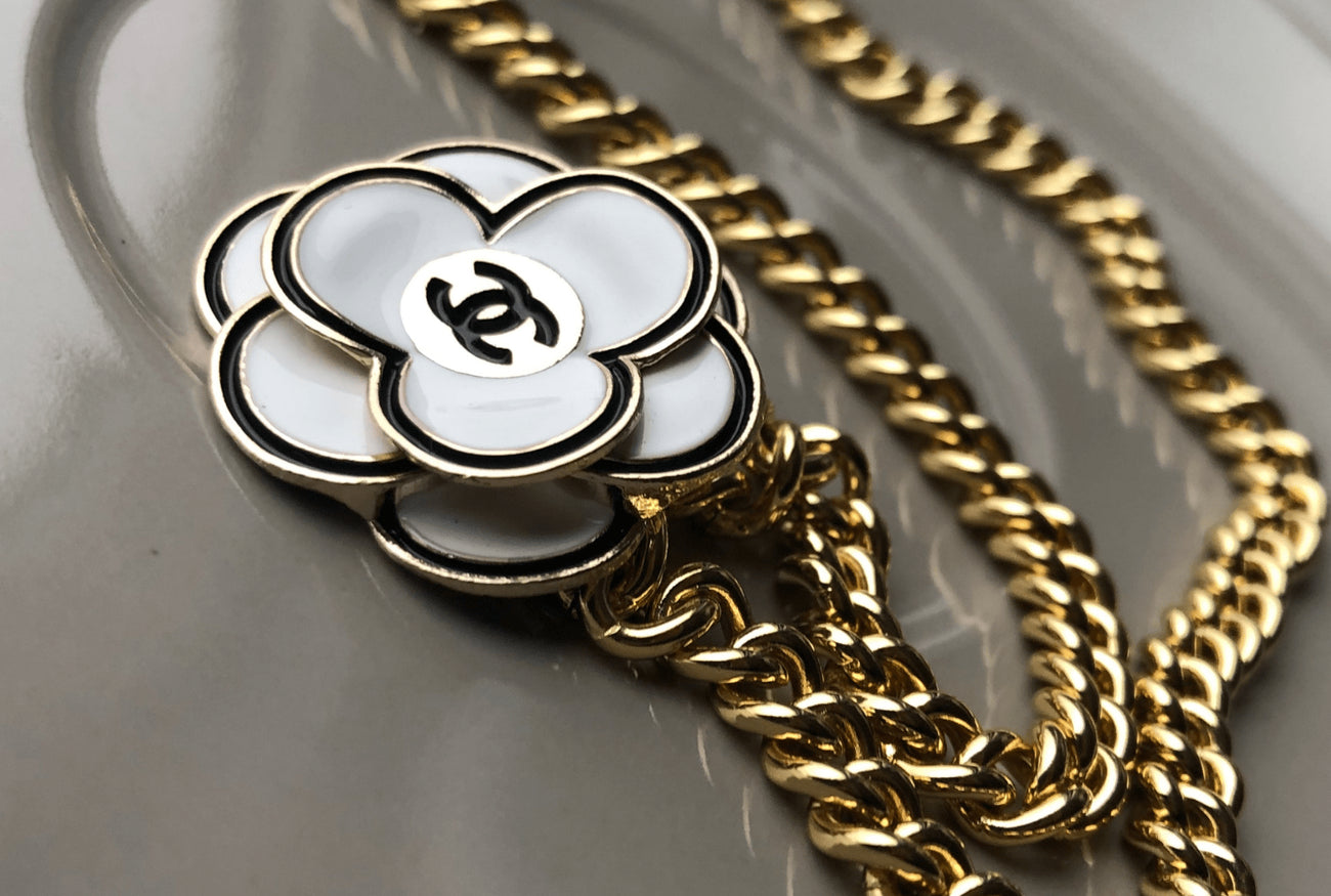 While enamel Chanel flower button repurposed into necklace on golf-filled curb chain.  Gives a classic vintage vibe.