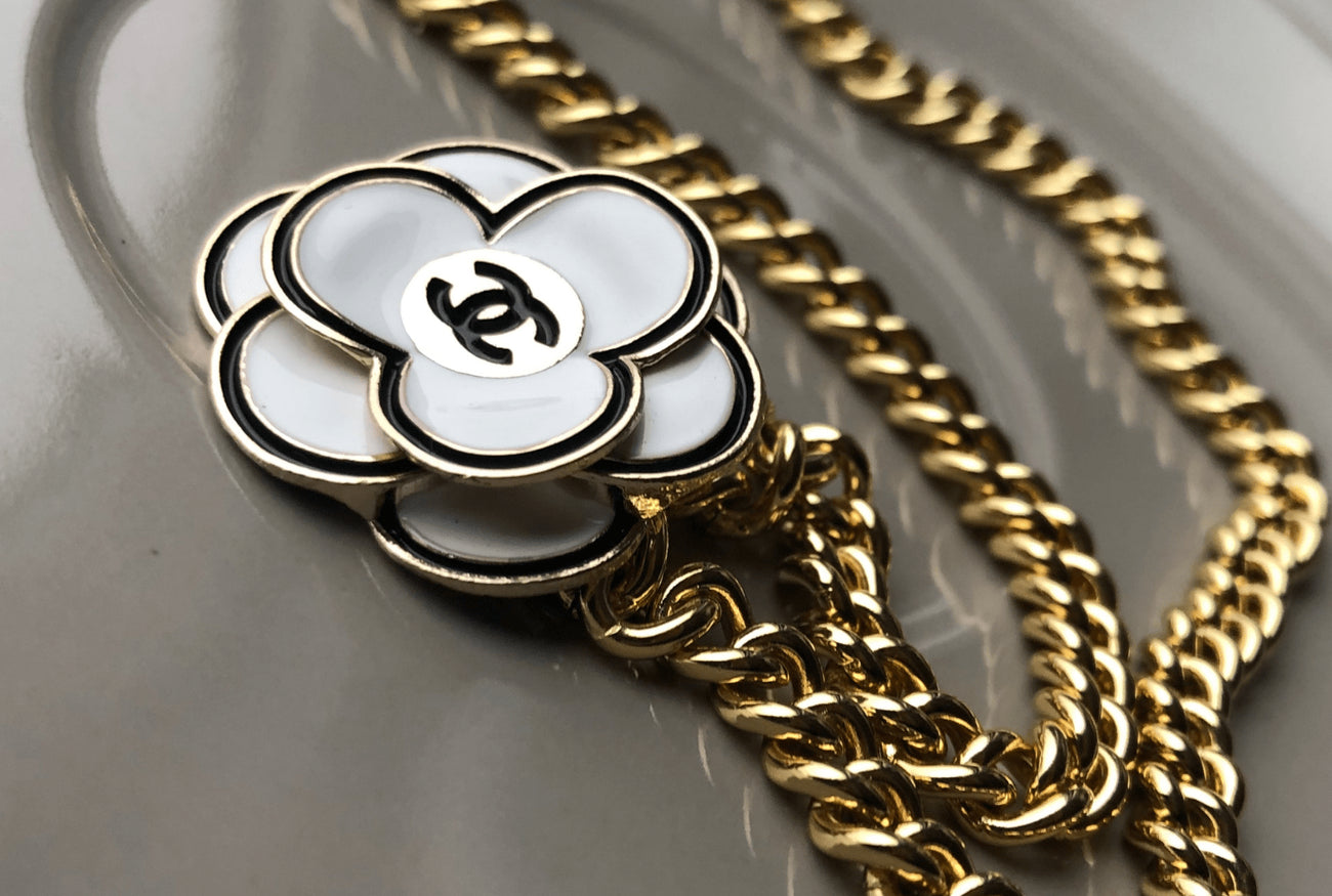 While enamel Chanel flower button repurposed into necklace on golf-filled curb chain.  Gives a classic vintage vibe. 